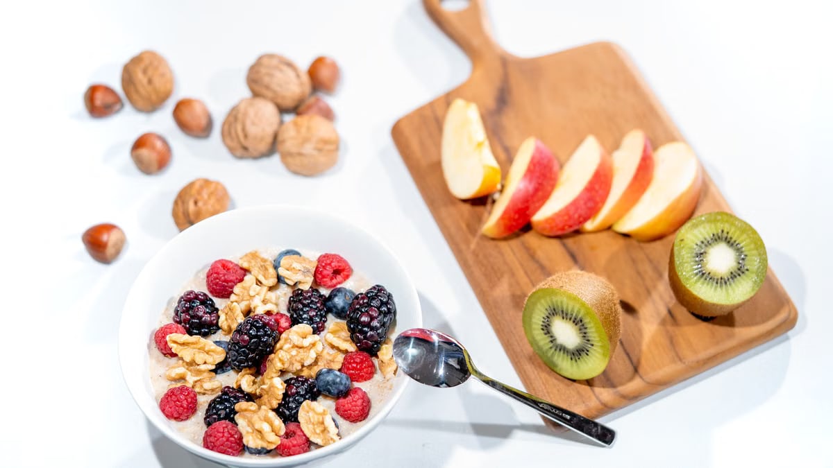 A nutritious breakfast bowl featuring fresh berries and walnuts, served with sliced fruit and kiwi.