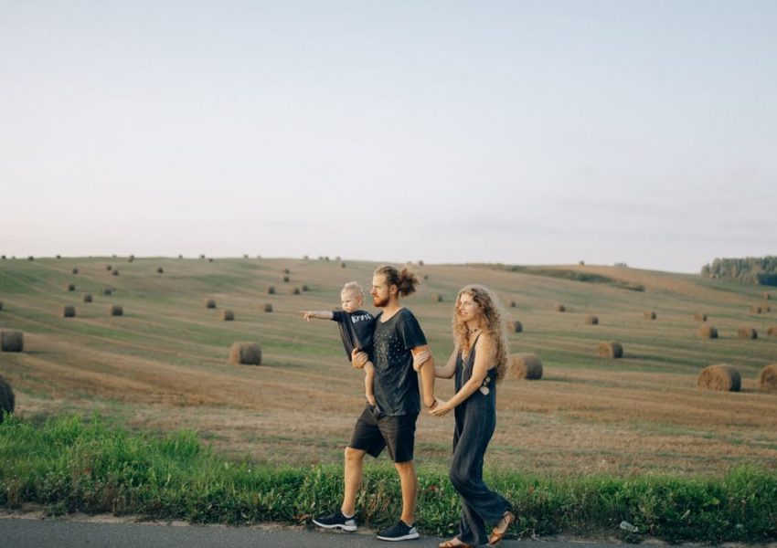 A joyful family walking hand in hand across a picturesque hayfield landscape at sunset.