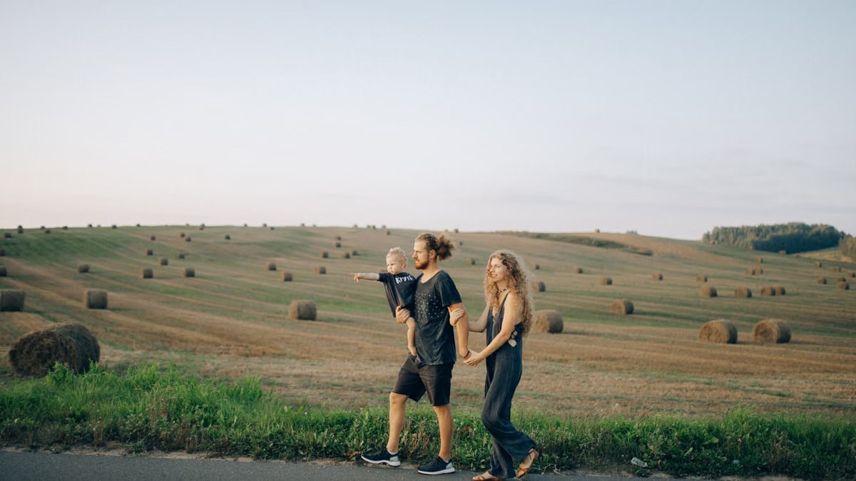 A joyful family walking hand in hand across a picturesque hayfield landscape at sunset.