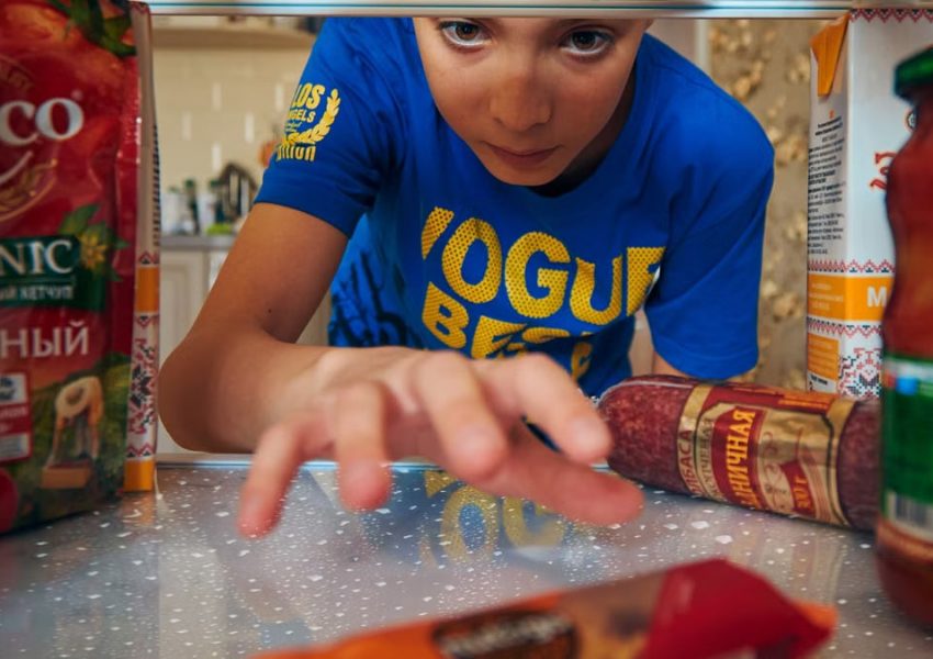 Young boy reaching into refrigerator for a snack. Close-up view indoors.
