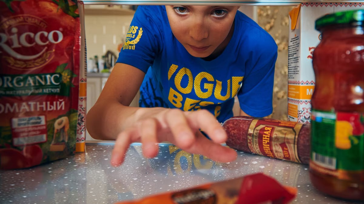 Young boy reaching into refrigerator for a snack. Close-up view indoors.